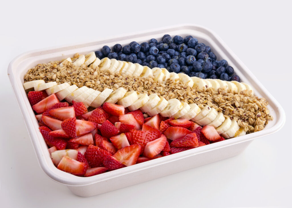 A colorful acai-based tray topped with strawberries, blueberries, banana slices, granola, and honey drizzle.