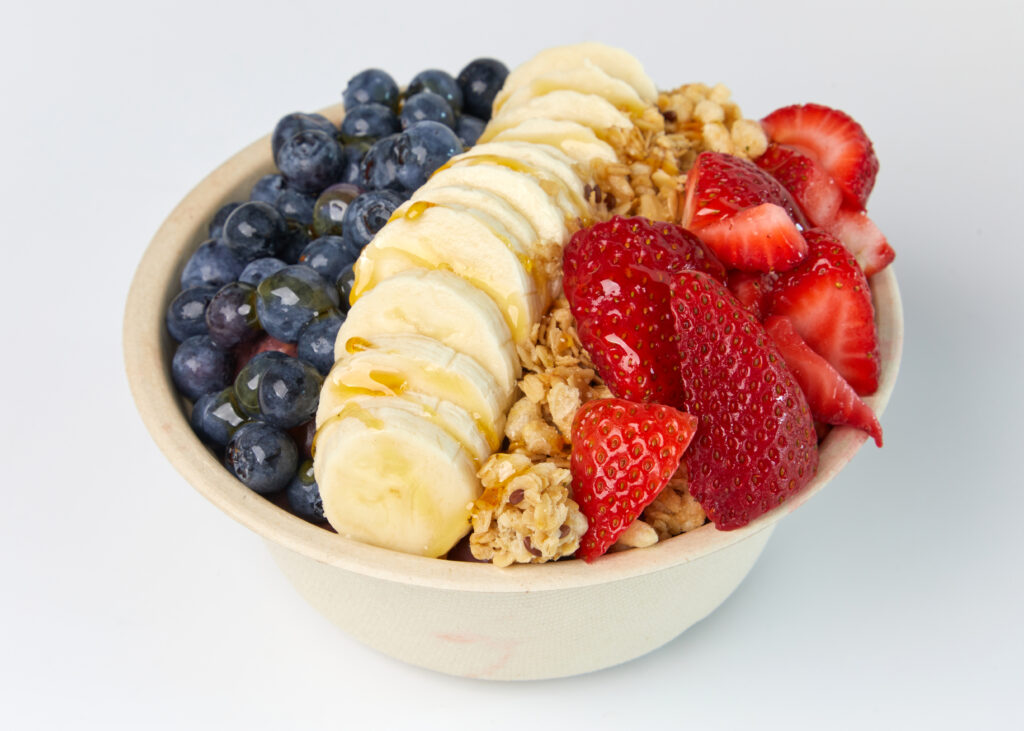 A smoothie bowl topped with bananas, strawberries, blueberries, granola, and honey drizzle.