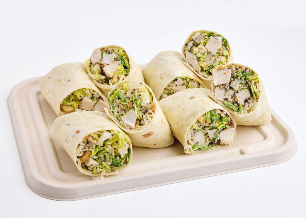 Halved chicken caesar wraps neatly arranged on a platter, filled with greens, quinoa, and parmesan.