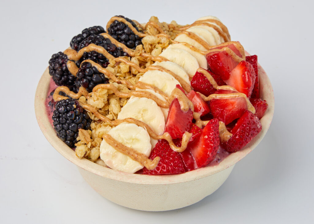 A colorful smoothie bowl with banana, strawberries, blueberries, almond butter, and crunchy granola.