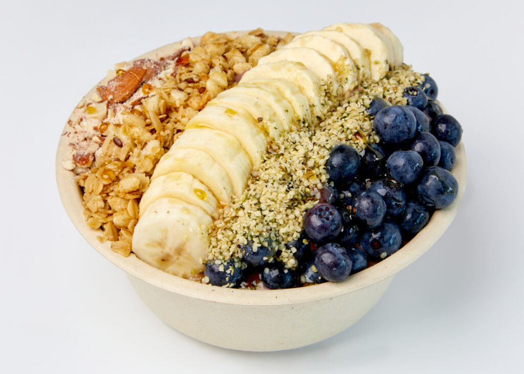 A protein-rich acai bowl with banana slices, blueberries, granola, hemp seeds, and almonds.