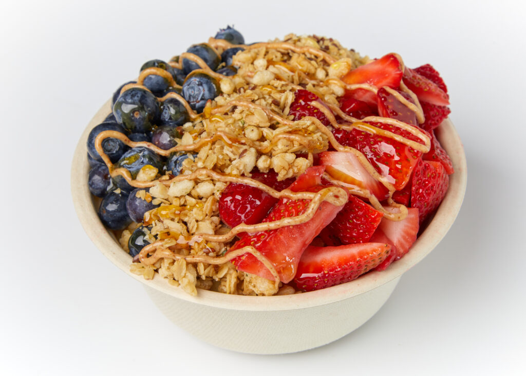 A fresh acai bowl topped with strawberries, blueberries, granola, almond butter, and honey.