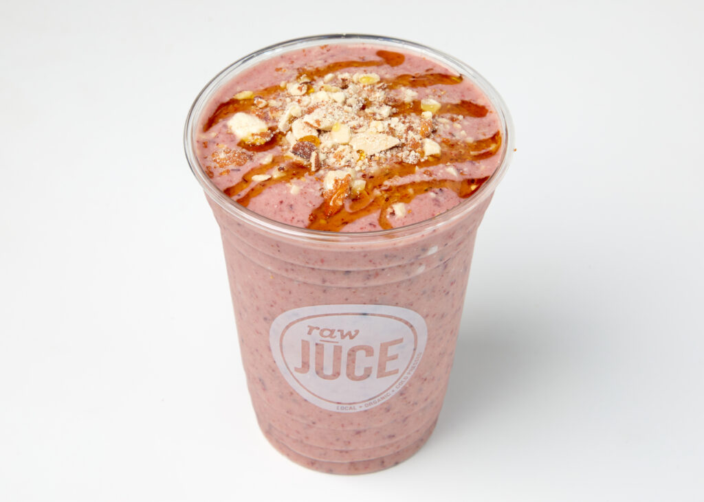 Four pink smoothies with almond butter, banana, and blueberry, garnished with almonds.