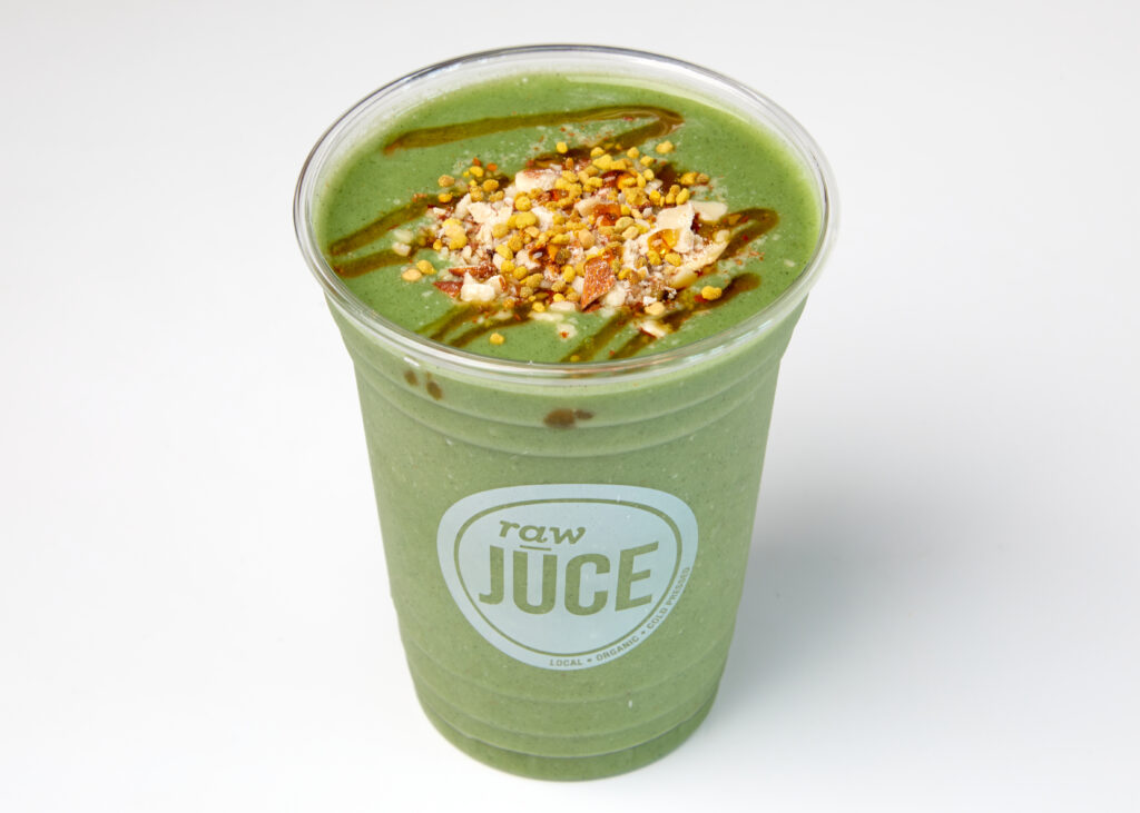 Four green smoothies in clear cups with protein, spinach, and almond toppings.